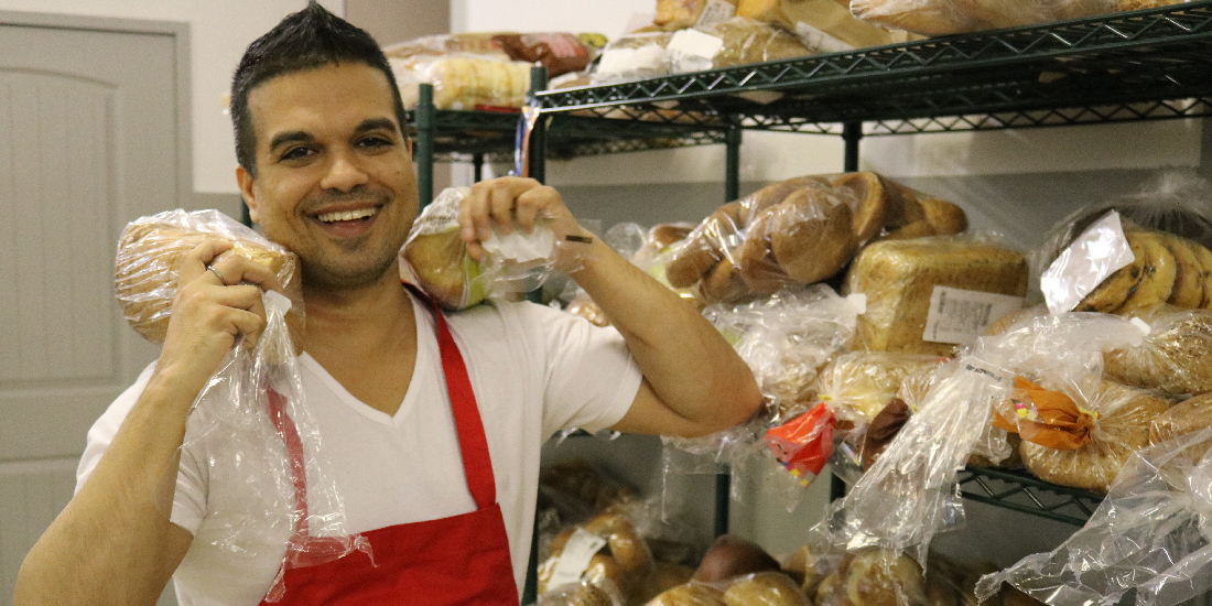 Smiling volunteer wearing a red apron holding loaves of bread in a food pantry.