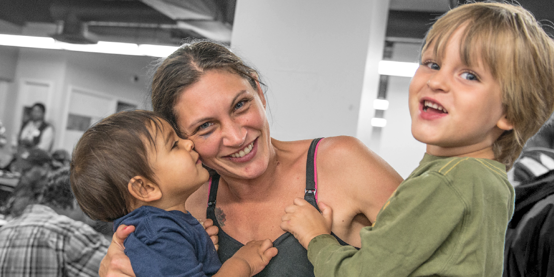 Smiling woman holding two happy young children.
