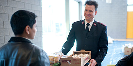 Salvation Army representative speaking with a community member while holding donated items.