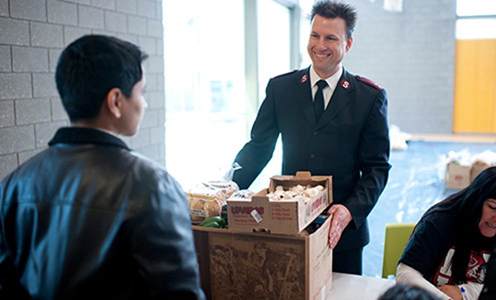 Salvation Army representative speaking with a community member while holding donated items.