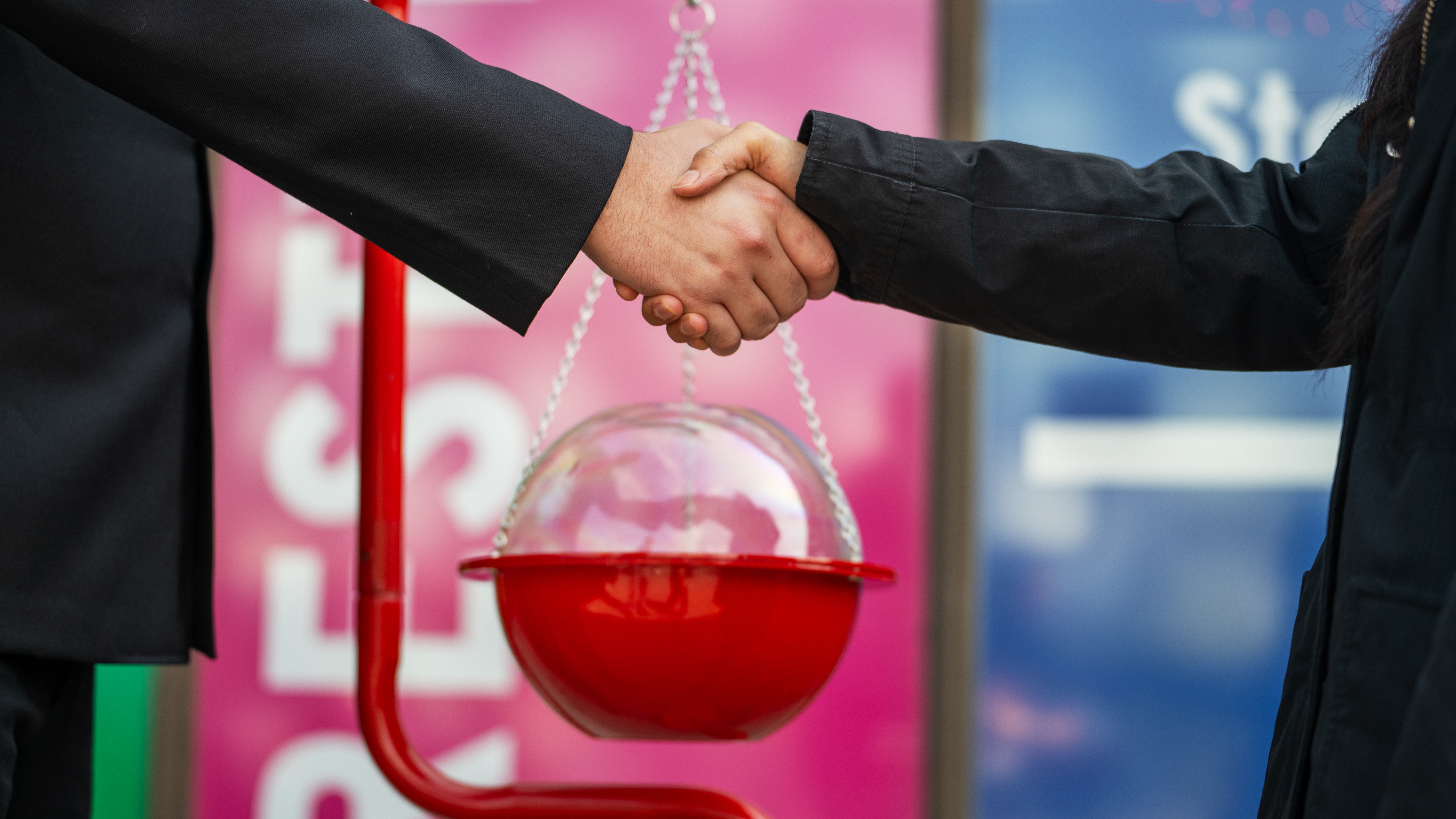 Close-up of two people shaking hands near a Salvation Army red kettle.