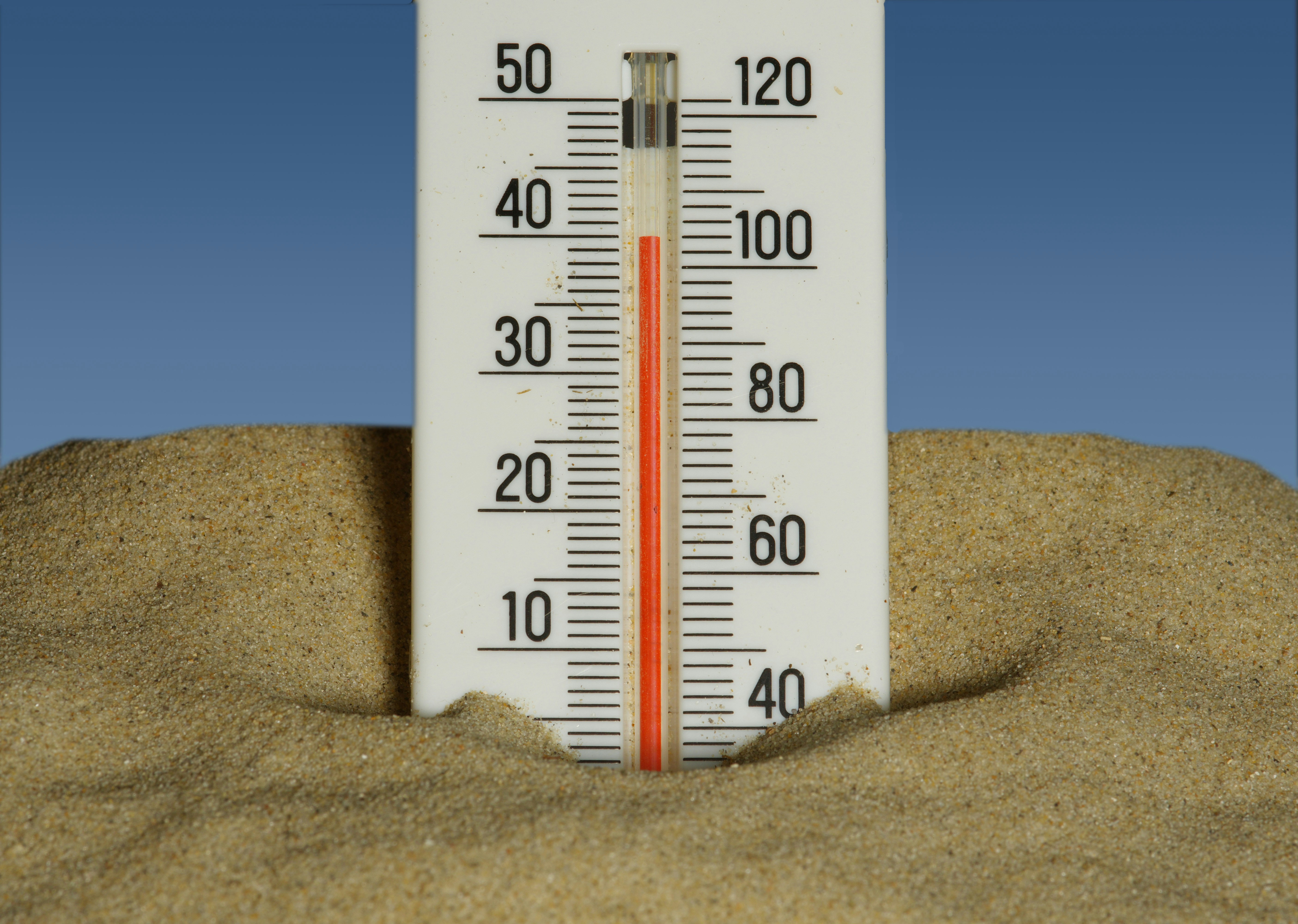 Thermometer partially buried in sand showing a high temperature