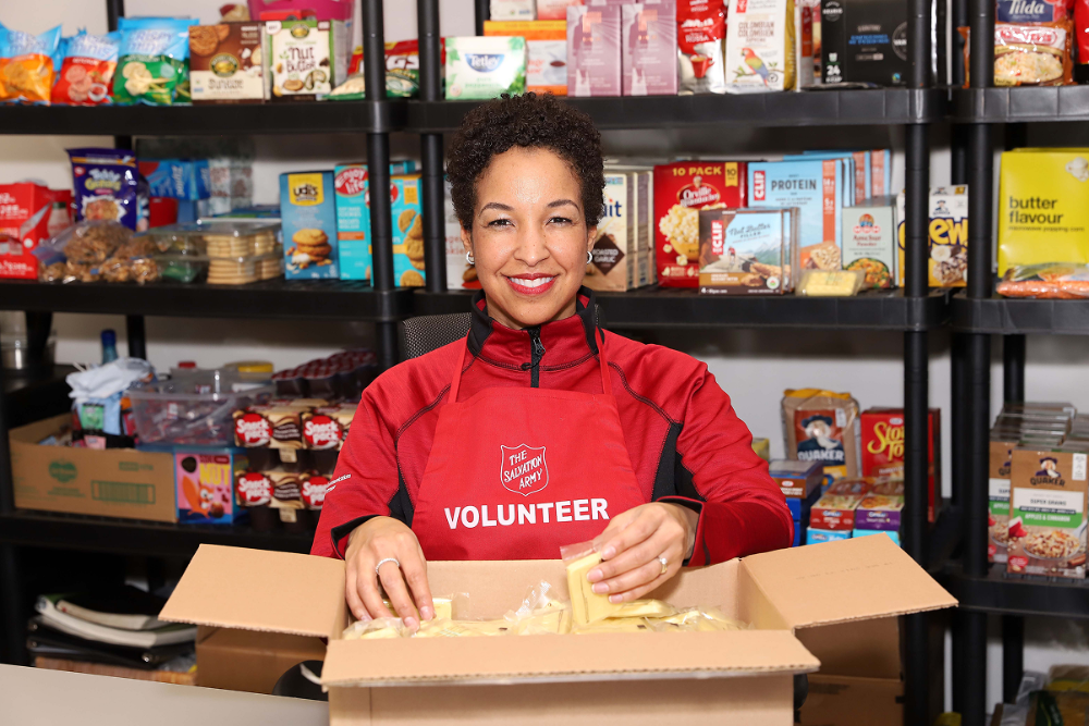Volunteer packing food items at a food bank, standing in front of stocked shelves.